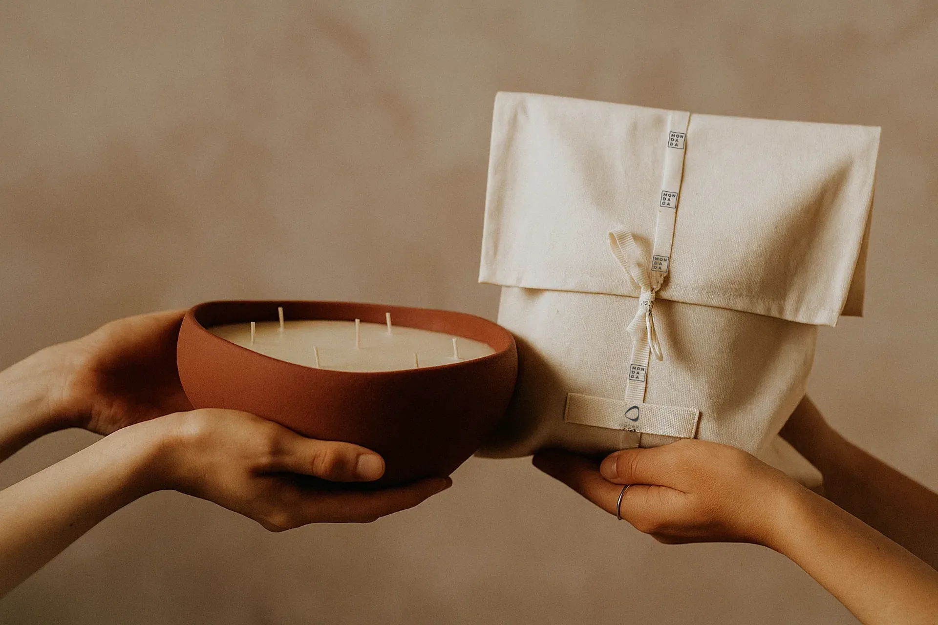 a hand holding a candle and another hand holding a linnen giftbag
