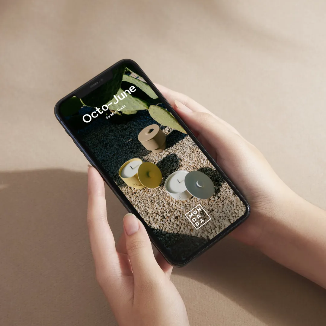 a hand holding a phone showing an advertisement of colourfull outdoor candles in front of a cactus